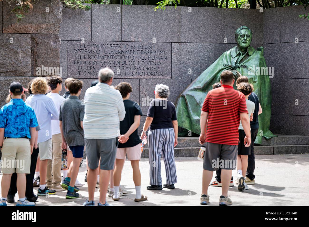 WASHINGTON DC - i visitatori si riuniscono con una guida turistica di fronte alla scultura in bronzo raffigurante il presidente Franklin D. Roosevelt seduto con il suo mantello e il suo terrier scozzese, Fala, al Franklin Delano Roosevelt Memorial. Il memoriale, progettato dall'architetto paesaggista Lawrence Halprin, è stato dedicato nel 1997 e si estende su 7,5 acri lungo il bacino di Tidal nel West Potomac Park. Questa scultura di Robert Graham rappresenta Roosevelt durante la sua presidenza (1933-1945) ed è una delle quattro sale all'aperto che raccontano i suoi quattro mandati in carica. L'inclusione di Fala rende questo l'unico animale domestico presidenziale raffigurato Foto Stock