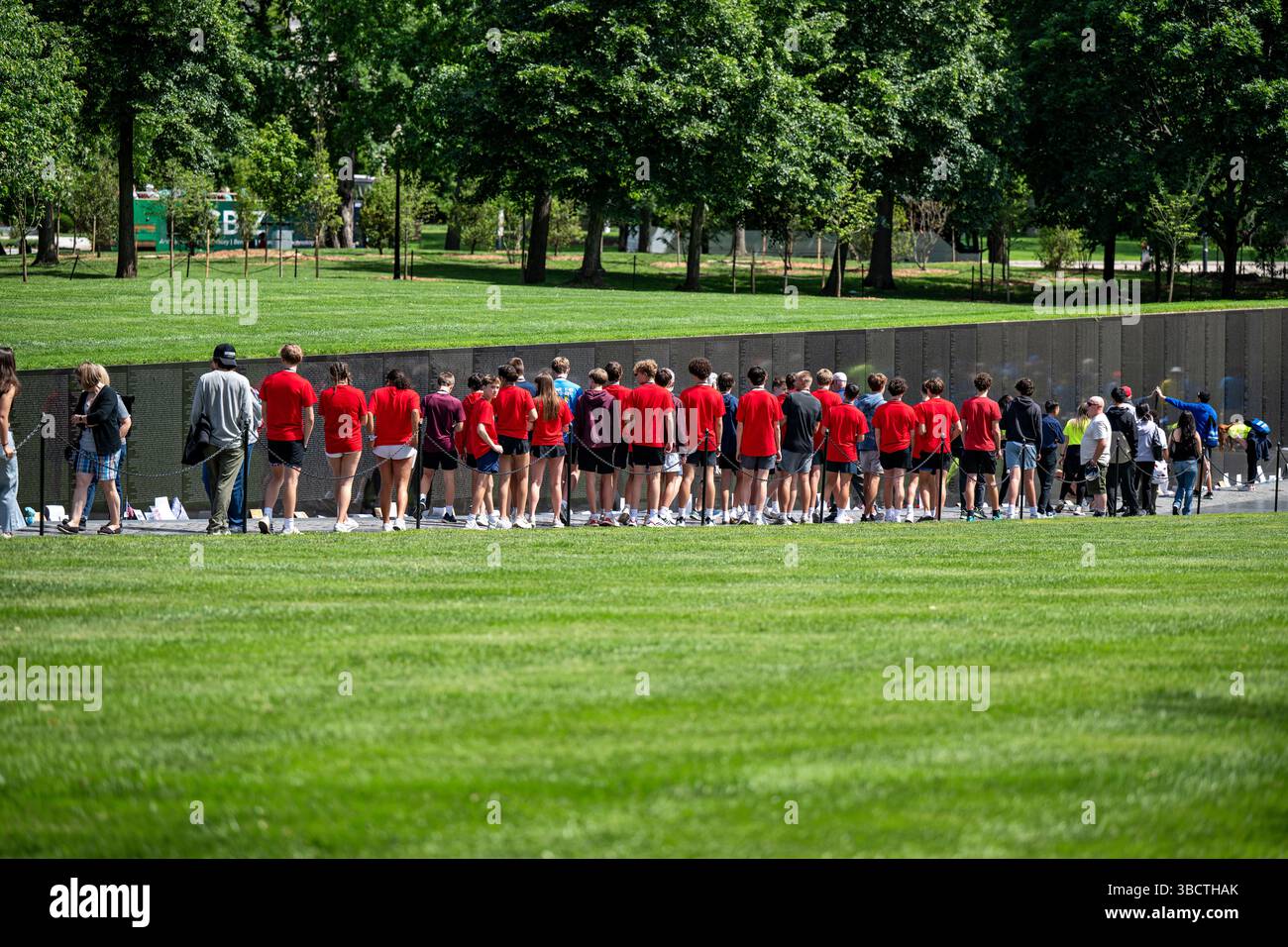 WASHINGTON DC - Un gruppo scolastico visita il Vietnam Veterans Memorial sul National Mall, un toccante luogo di commemorazione della guerra del Vietnam. Progettato da Maya Lin e dedicato nel 1982, il memoriale presenta una parete di granito nero riflettente con incisi i nomi di oltre 58.000 membri del servizio militare americano che sono morti o scomparsi durante il conflitto. Gli studenti spesso si impegnano in attività educative, come rintracciare i nomi e conoscere l'impatto della guerra sulla storia americana. Foto Stock