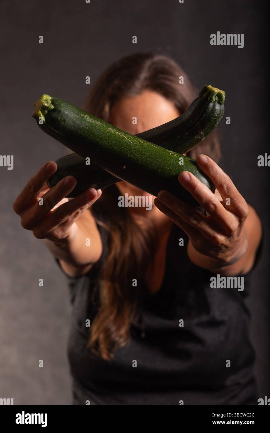 Una donna ha due zucchine fresche davanti a lei. Le zucchine sono di colore verde scuro e disposte a croce. L'attenzione e' sulle zucchine, arguto Foto Stock