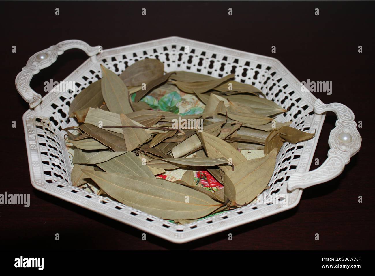Un cestino bianco decorativo con manici decorati con perle. All'interno del cestello sono presenti numerose foglie di alloro essiccate sparse sul fondo. Foto Stock