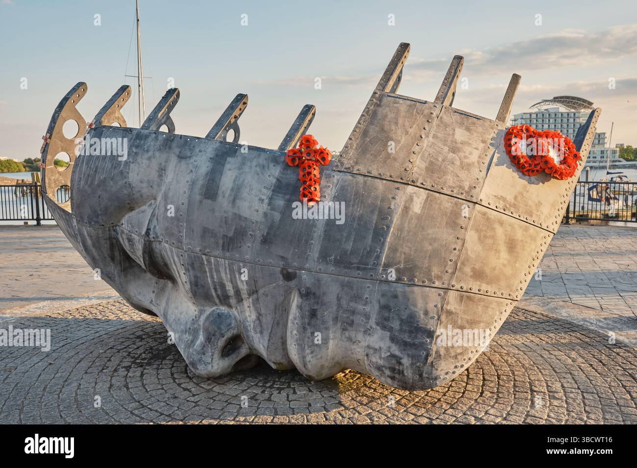 Commemorazione della guerra dei marinai mercanti nella baia di Cardiff, un'impressionante scultura in bronzo di un volto caduto e di uno scafo della nave adornato da ghirlande di papavero al tramonto. Foto Stock