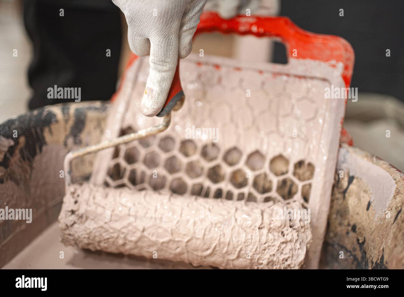 L'uomo immerge un rullo per pittura per rimuovere la vernice in eccesso dal tergivetro. Foto Stock