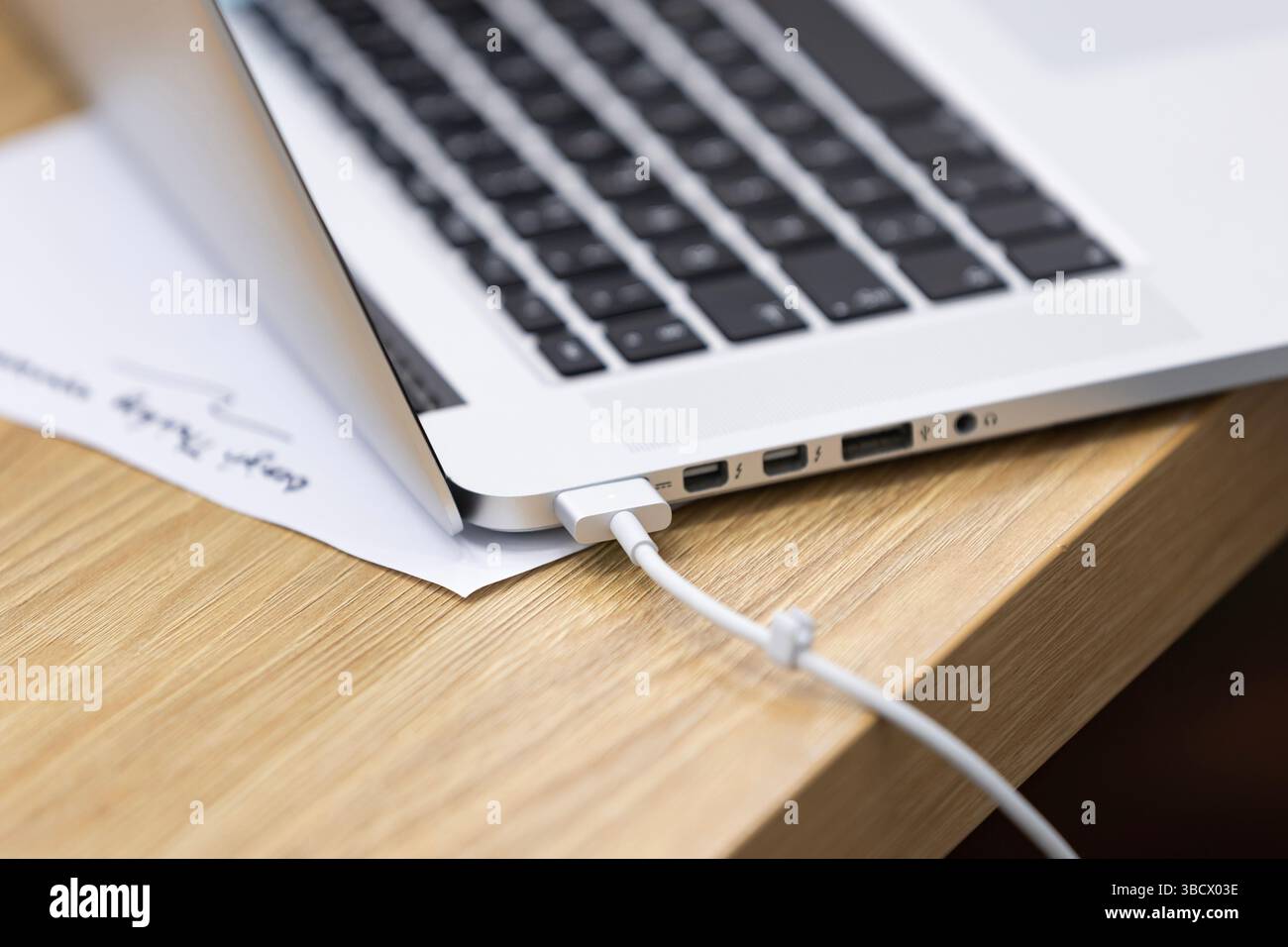 Ricarica di un computer portatile su una scrivania in legno: Lavora da casa o da ufficio. Foto Stock