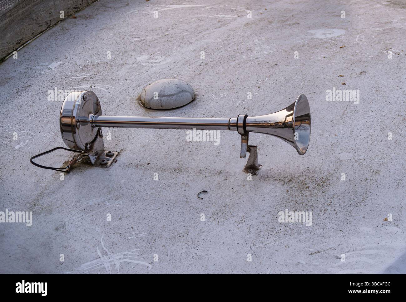 Un corno metallico montato su una base, appoggiato su una superficie ruvida. Il clacson ha una finitura lucida ed è collegato a un filo, suggerendo che potrebbe essere parte di Foto Stock