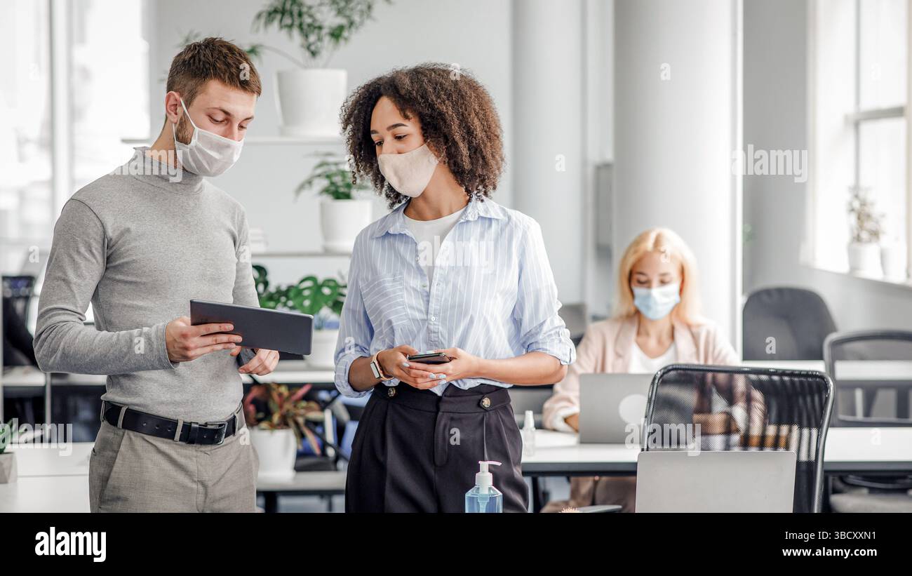 Idee di marketing per il lavoro e la protezione contro le epidemie. Il manager mostra la signora afroamericana in un tablet con maschera protettiva con un compito vicino al posto di lavoro Foto Stock