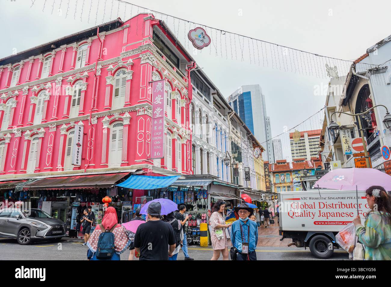 Singapore, Singapore - 4 aprile 2025: Colorati edifici coloniali e vita di strada a Little India. Persone che camminano con gli ombrelli in una giornata di pioggia in una vi Foto Stock