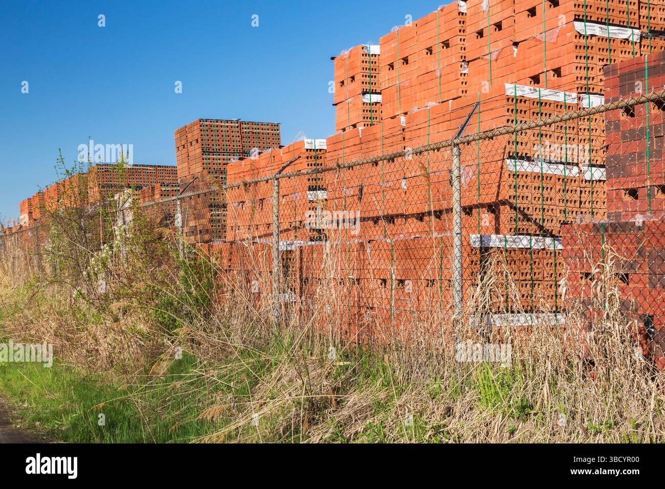 Fasci legati di mattoni di argilla rossa impilati ordinatamente in un deposito all'aperto in primavera. Foto Stock