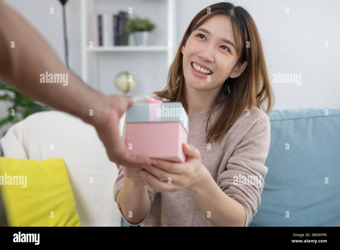 La bella donna asiatica si sente sorpresa e guarda la confezione regalo di interesse. una bella ragazza entusiasta di aprire la confezione regalo. Compleanno, festa, Natale, Capodanno, grazie, C Foto Stock