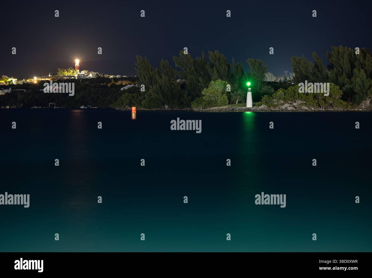 Faro di navigazione e faro distante di notte sulla costa delle Bermuda, con superficie d'acqua liscia sotto lunga esposizione e luci della costa. Foto Stock Faro di navigazione e faro distante di notte sulla costa delle Bermuda, con superficie d'acqua liscia sotto lunga esposizione e luci della costa. Foto Stock