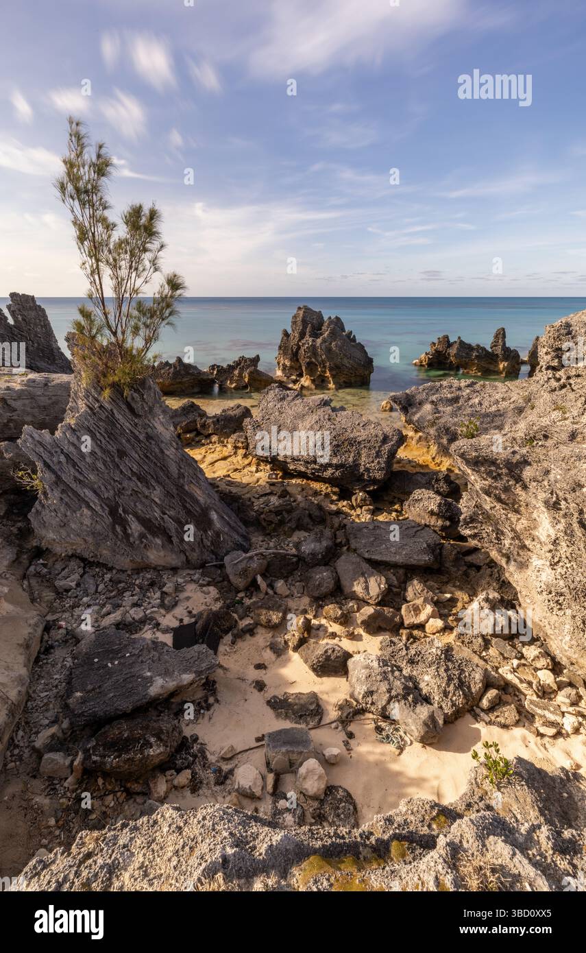 Paesaggio verticale di costa rocciosa e mare turchese alle Bermuda, con formazioni calcaree, sabbia e nuvole a lunga esposizione sotto il cielo blu. Foto Stock