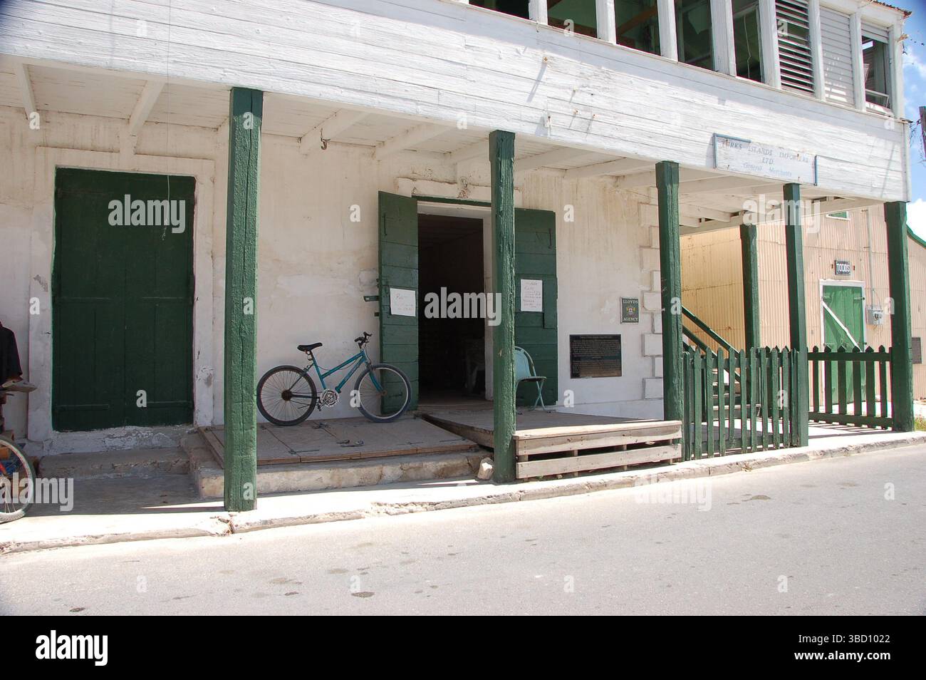 Vecchio edificio in stile coloniale con persiane verdi e portico, caratterizzato da una bicicletta blu parcheggiata all'esterno in una strada tranquilla a Grand Turk Foto Stock