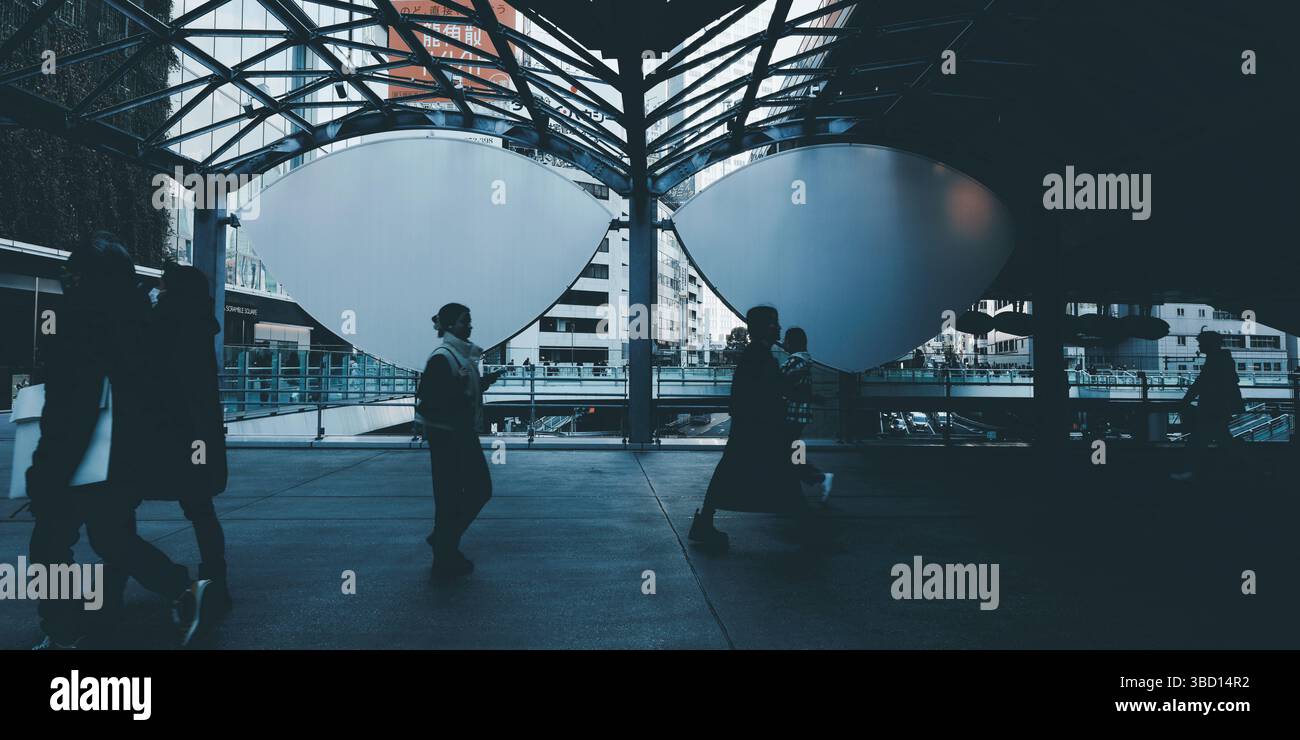 I pendolari attraversano la passerella Shibuya Stream, incorniciata da un'audace architettura in acciaio e da una luce urbana soffusa Foto Stock