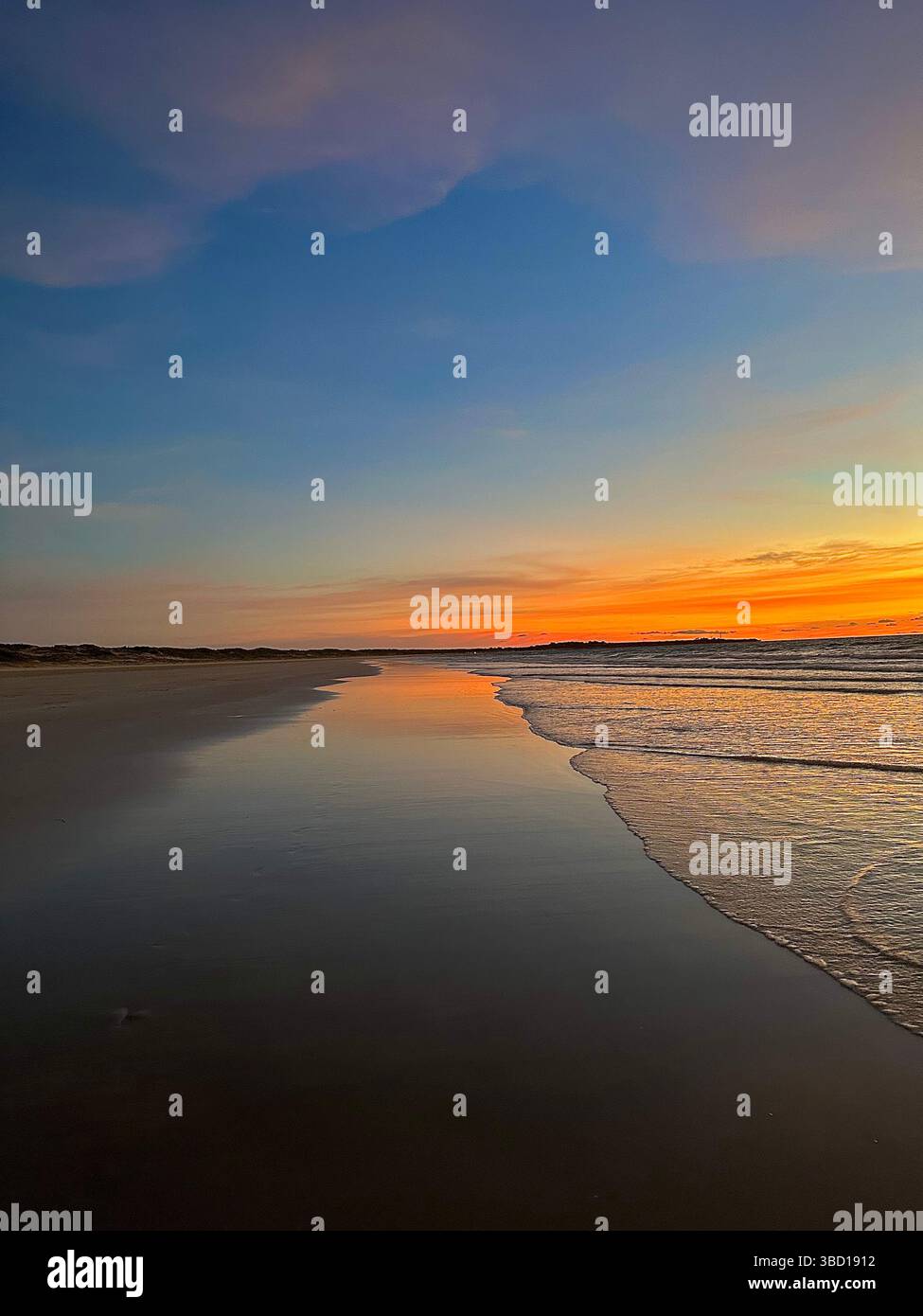 Spiaggia tranquilla al tramonto con onde dolci e vibranti riflessi del cielo sulla sabbia bagnata, perfetta per viaggi, benessere e concetti di stile di vita. - Immagine stock catturata con smartphone