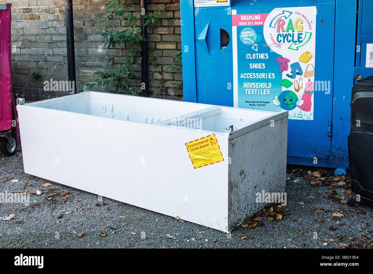 Un frigorifero rotto, che è un grande apparecchio elettrico, viene scaricato illegalmente accanto al cestino di riciclaggio del piccolo apparecchio. Concetto: Fly-tipping Foto Stock