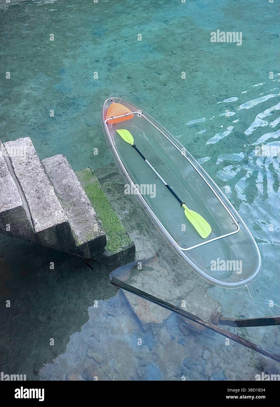 Kayak trasparente con pagaie gialle che galleggiano sulle acque turchesi accanto ai gradini di pietra, ideale per viaggi, avventura ed eco-turismo. - Immagine stock catturata con smartphone