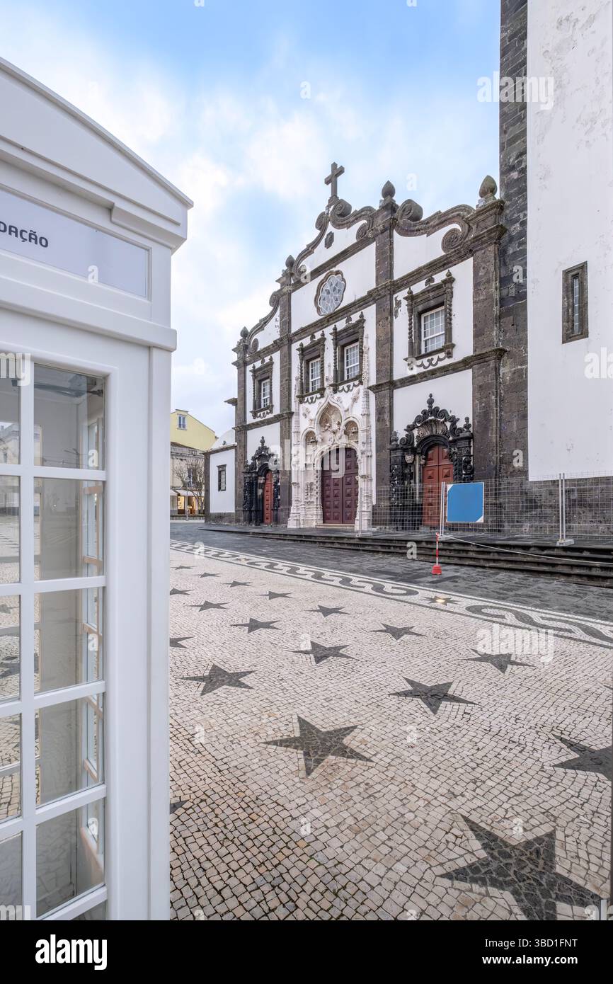Facciata principale dell'Igreja de Sao Sebastiao con lastricato portoghese Star Pattern a Ponta Delgada. La chiesa barocca delle Azzorre e la cabina telefonica convertita in Littl Foto Stock