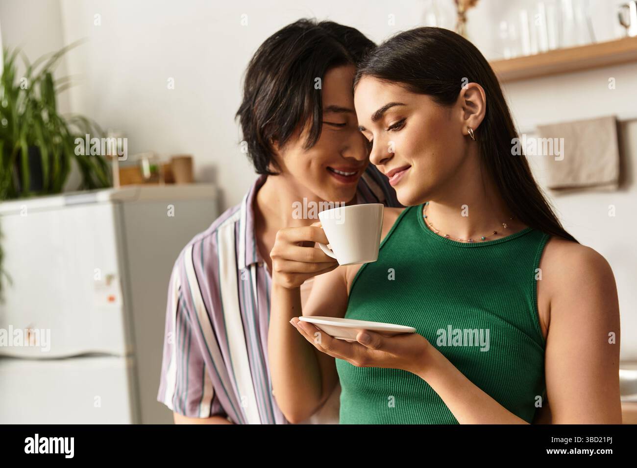 Una coppia gioiosa si gode un momento tenero a casa, condividendo caffè e sorridendo con calore. Foto Stock