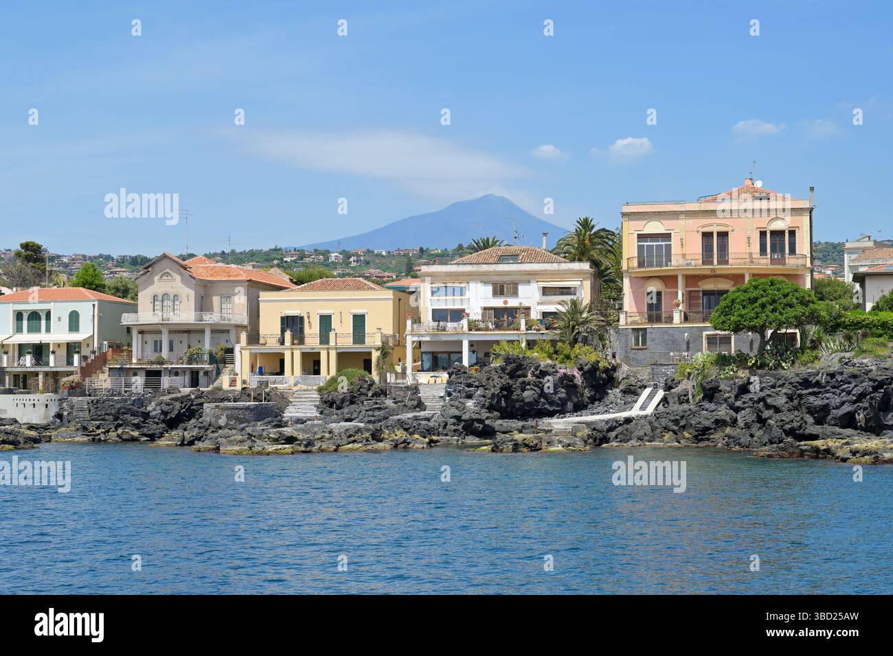 ACI Castello, Sicilia, Italia - 3 maggio 2025 - pittoresche case siciliane durante una gita in barca con il vulcano Etna fumante sullo sfondo del cielo blu. Foto Stock