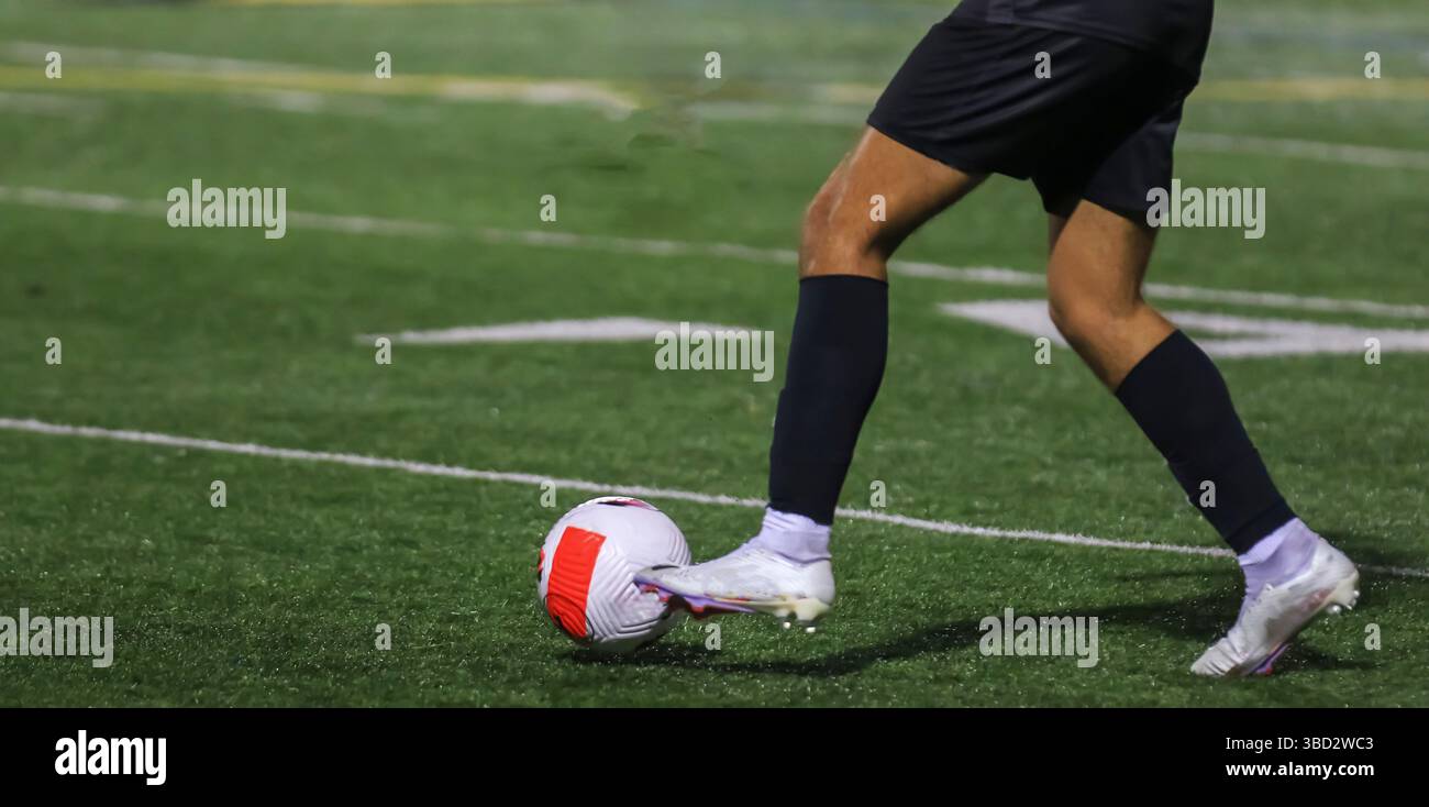 Un giocatore con equipaggiamento nero colpisce abilmente una palla da calcio su un tappeto erboso ben tenuto. Foto Stock