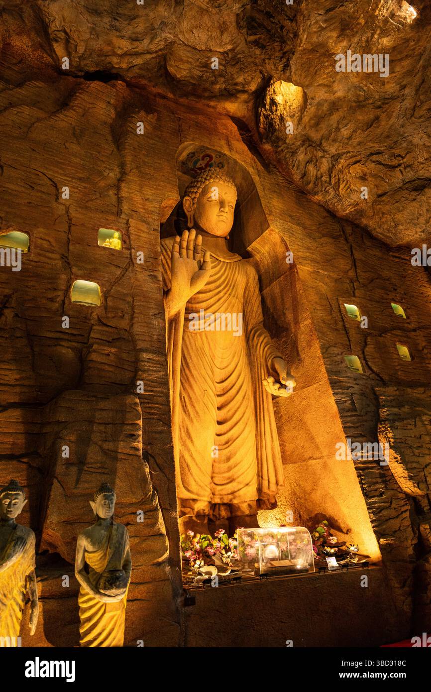 Una maestosa statua dorata di Buddha scolpita nella parete della grotta di un tempio tailandese, delicatamente illuminata per rivelare le intricate texture e l'atmosfera sacra. Foto Stock