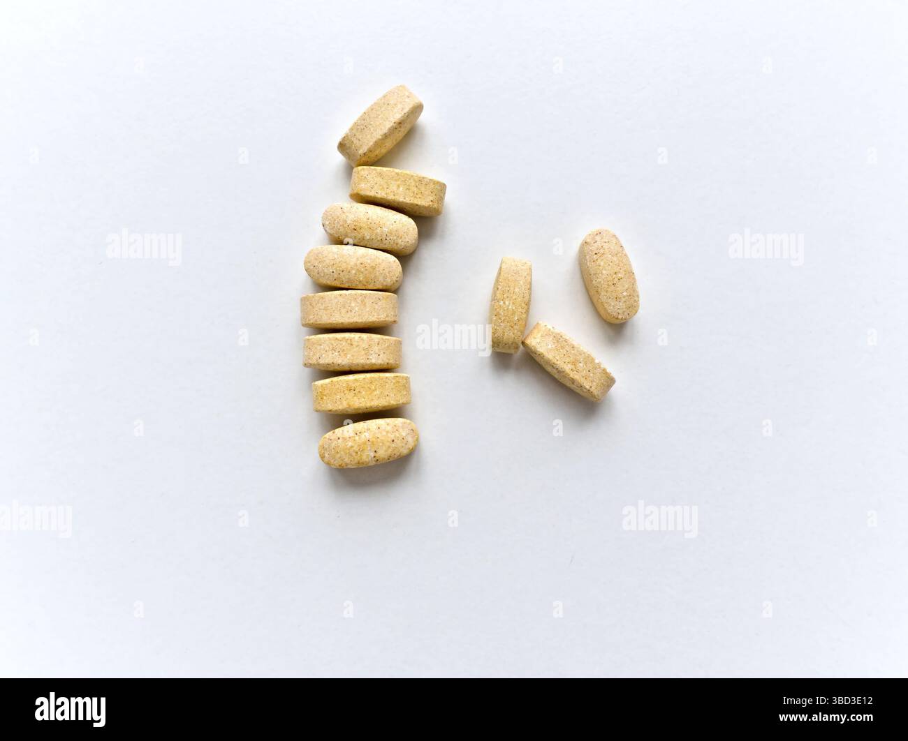 Un mucchio di pillole si stendono su uno sfondo bianco. Le pillole sono gialle e sembrano avere la forma di un rettangolo Foto Stock