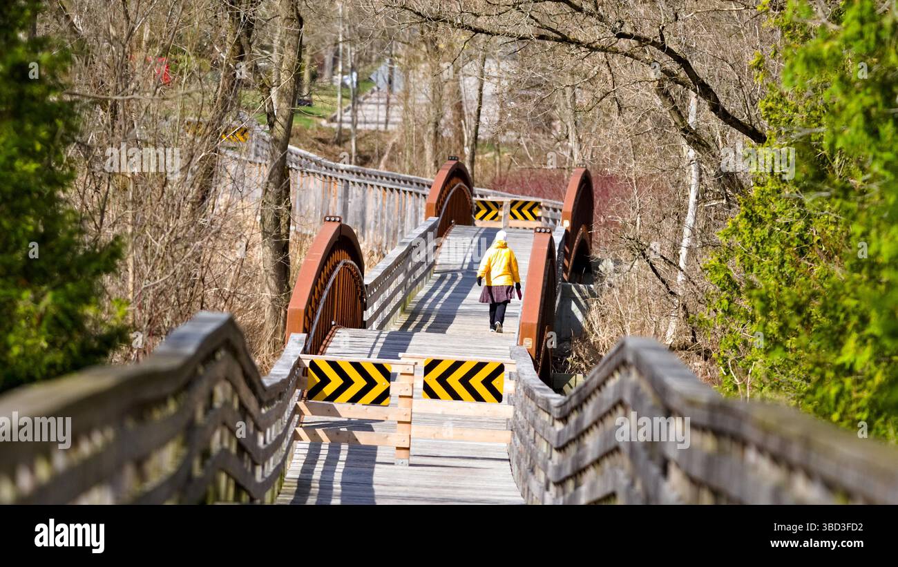 Una donna sta attraversando un ponte con una giacca gialla. Il ponte è chiuso con un cartello giallo e nero Foto Stock