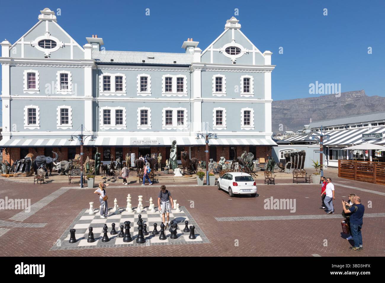 I turisti sono a scacchiera all'aperto di fronte al negozio African Trading Port ospitato nell'Old Port Captain's Building, V&A Waterfront, città del Capo Foto Stock