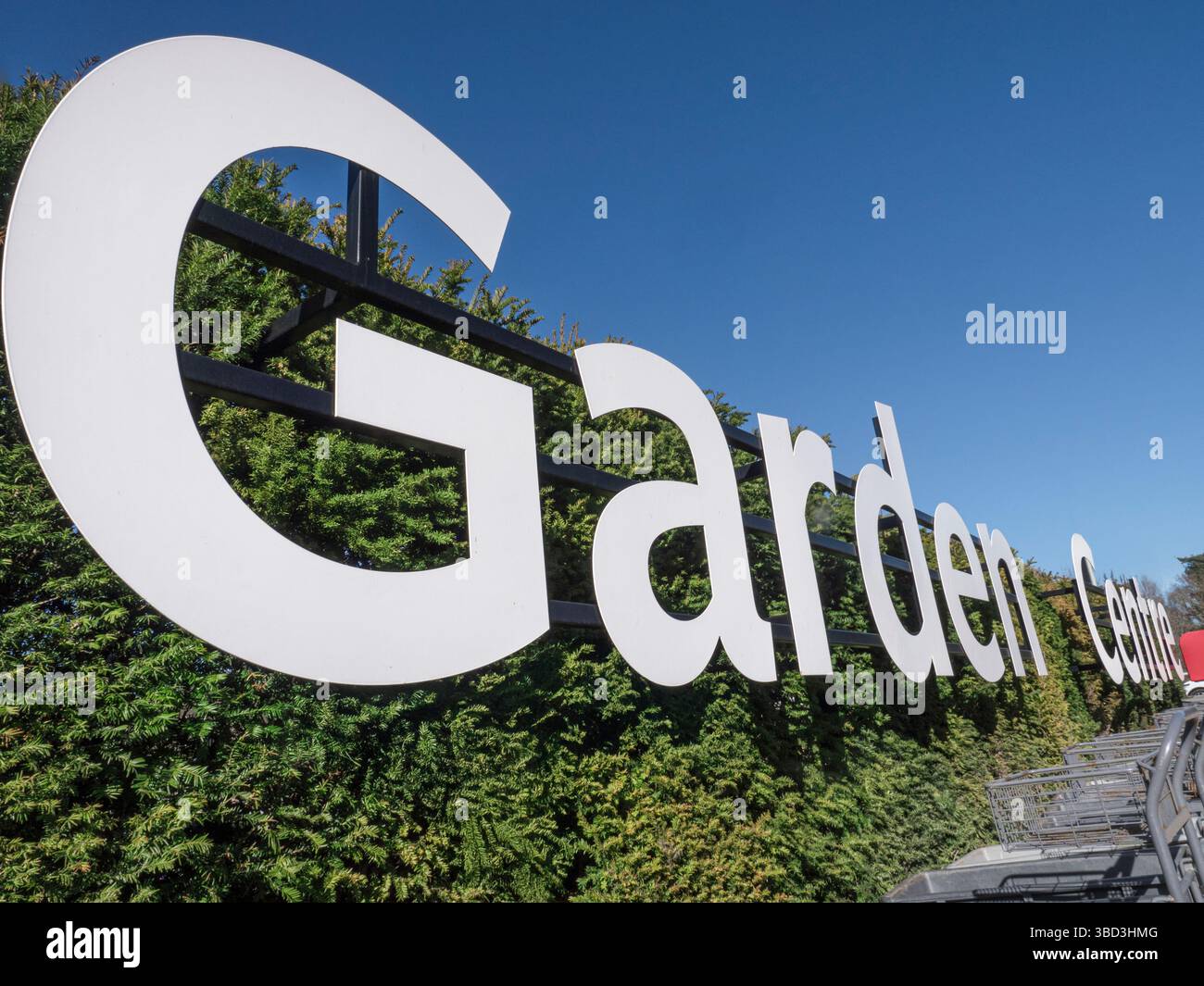 Insegna bianca grafica Garden Centre, con il sole primaverile e i carrelli delle piante in primo piano. Surrey Regno Unito Foto Stock