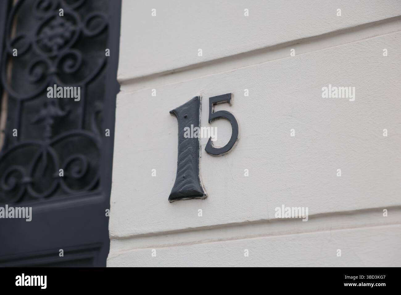 Un numero di metallo nero "15" è fissato su una parete bianca liscia, che funge da indicatore di indirizzo chiaro. Foto Stock