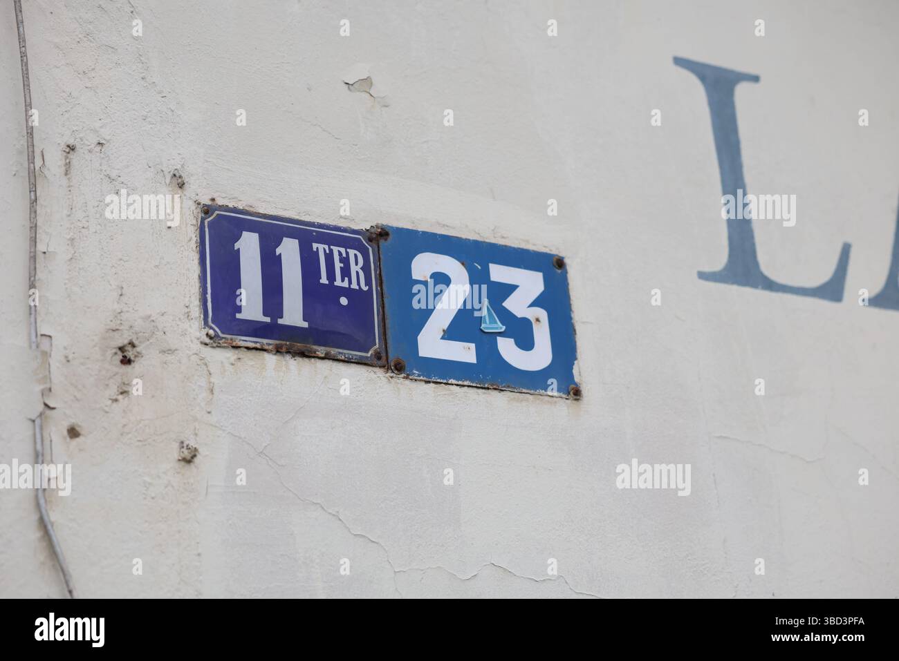 Su una parete bianca sono apposti due segnali con numero civico con crepe visibili e vernice sbucciante. Il segno a sinistra recita “11 ter” in testo bianco su un blu Foto Stock