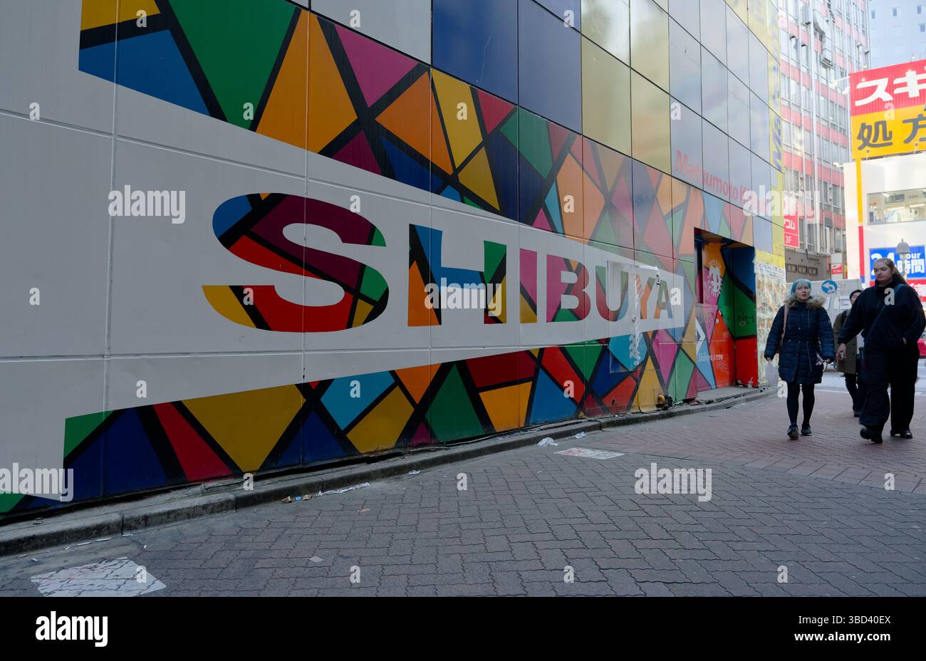 Il colorato murale geometrico indica con audacia "Shibuya" mentre i pedoni passano Foto Stock