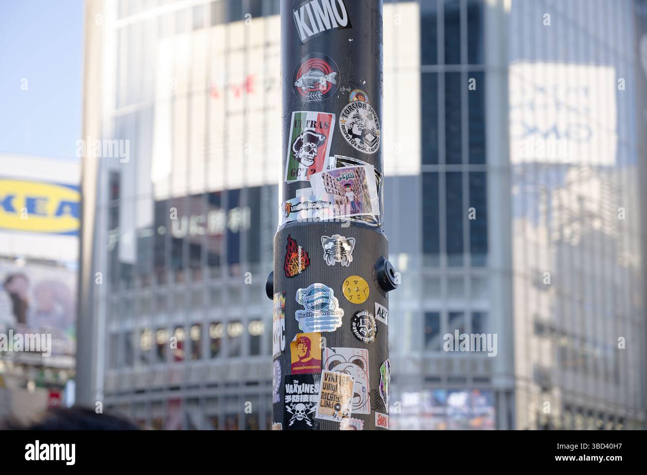 Il palo rivestito di adesivi si staglia tra le torri di vetro di Shibuya Foto Stock
