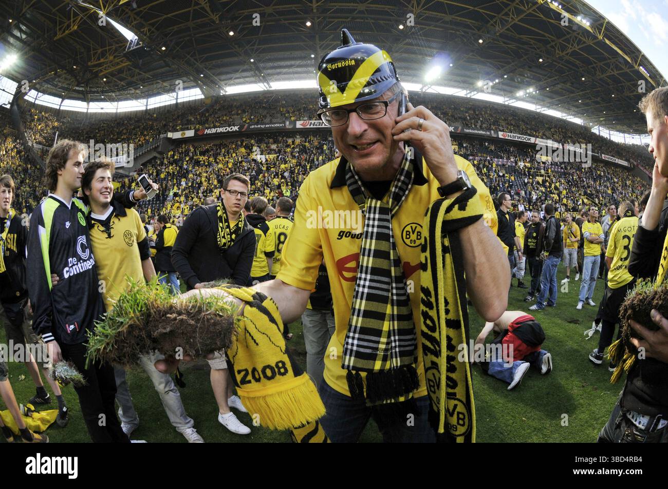 Celebrazione del campionato Borussia Dortmund, un fan con casco a spillo e un pezzo di prato in mano che parla al telefono con entusiasmo, prato di Foto Stock