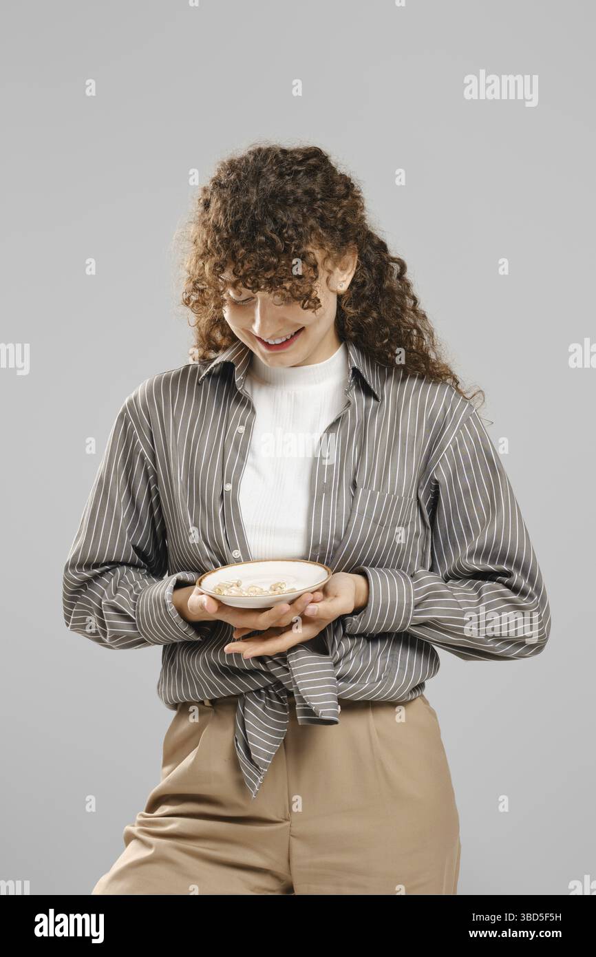 Una donna sorridente tiene in mano un piatto pieno di pillole Foto Stock