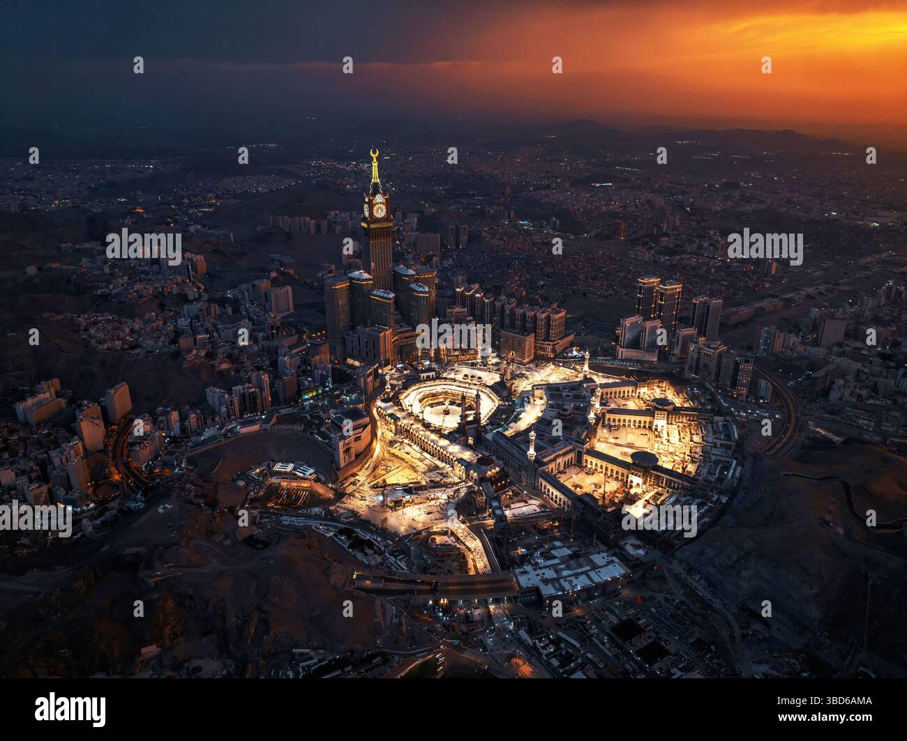 Veduta aerea notturna della grande Moschea illuminata e della Torre dell'Orologio della Mecca, che mostra il vibrante bagliore della città mentre le luci brillano attraverso il sito sacro Foto Stock