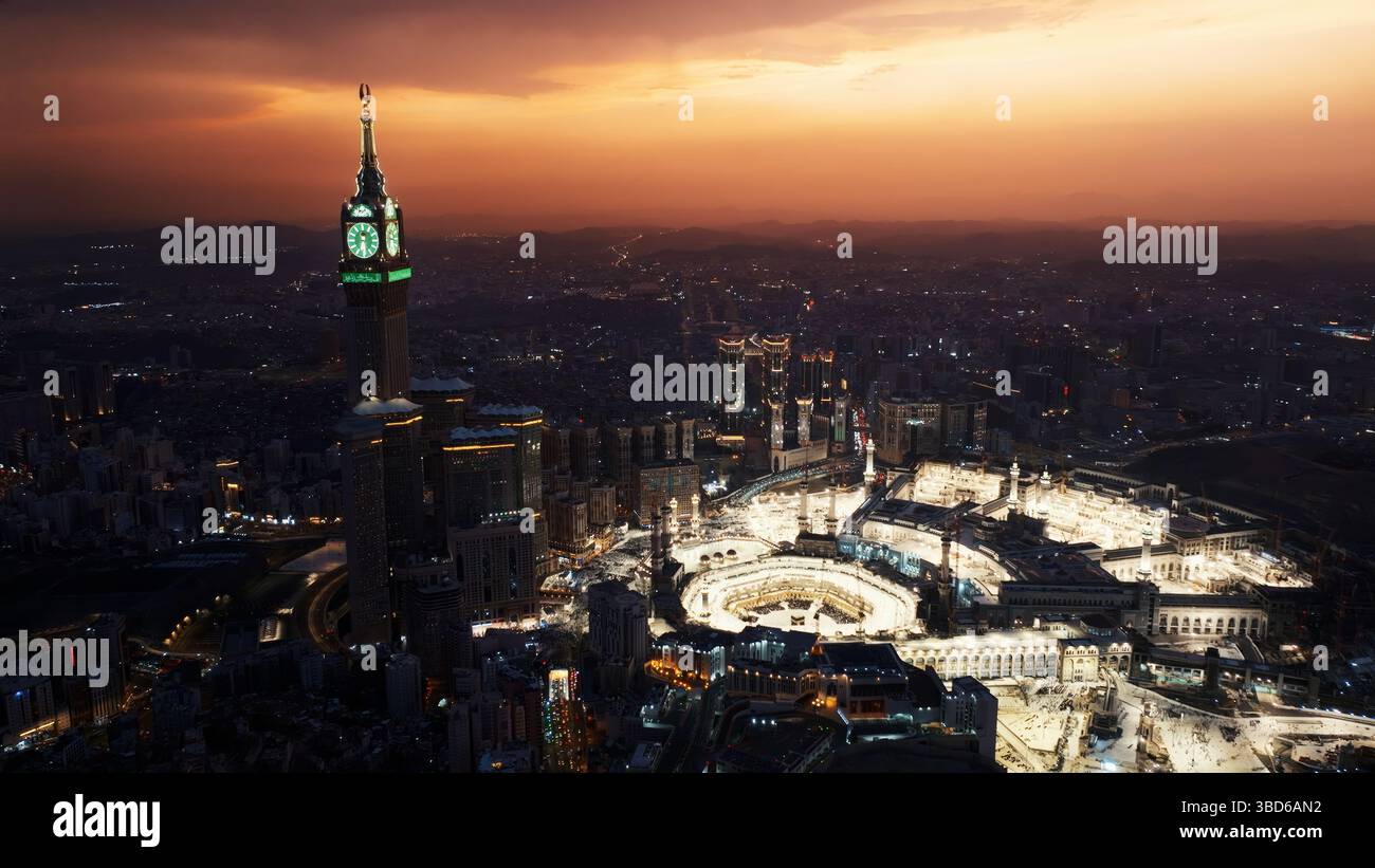 Veduta aerea notturna della grande Moschea illuminata e della Torre dell'Orologio della Mecca, che mostra il vibrante bagliore della città mentre le luci brillano attraverso il sito sacro Foto Stock