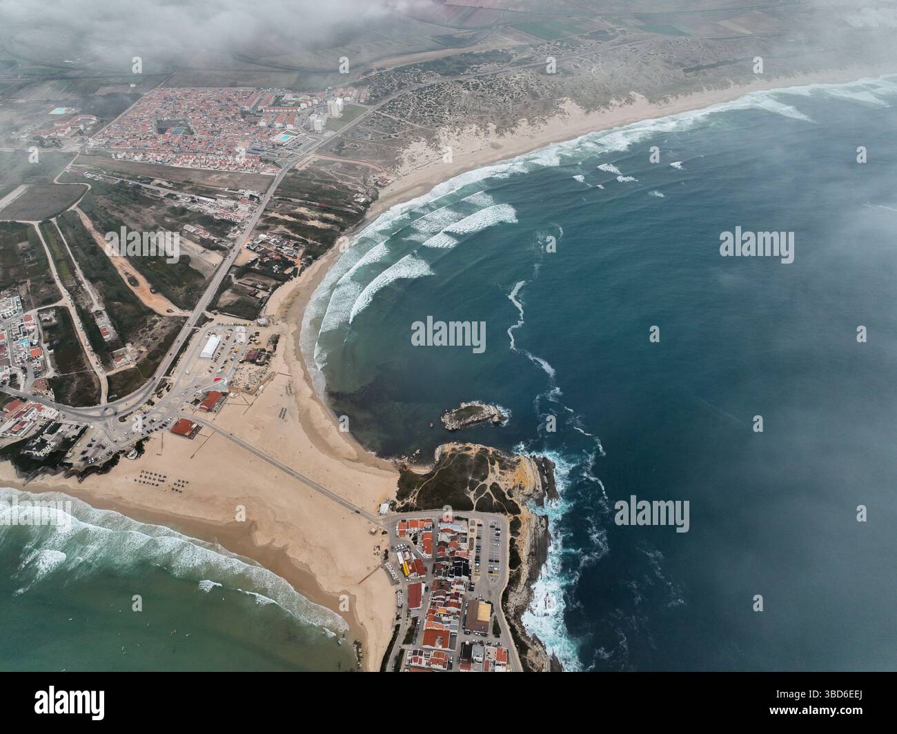 Ampia antenna che mostra la curvatura della spiaggia, le onde e la città che si estende nell'entroterra Foto Stock
