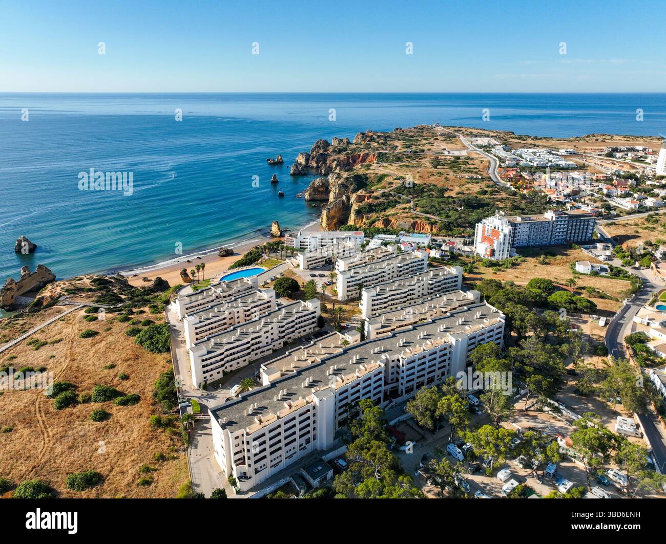 Edifici costieri vicino alle scogliere panoramiche dell'Algarve e alla spiaggia con un oceano blu profondo sotto il cielo limpido Foto Stock