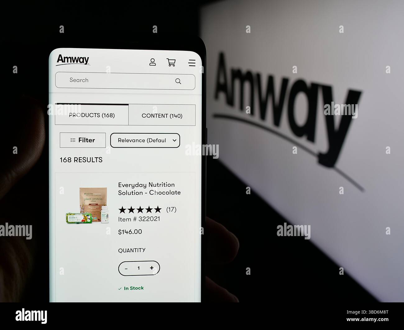 In questa immagine, una persona ha in mano un cellulare con la pagina Web della società di marketing multilivello statunitense Amway Corp. Sullo schermo davanti al logo. Foto Stock