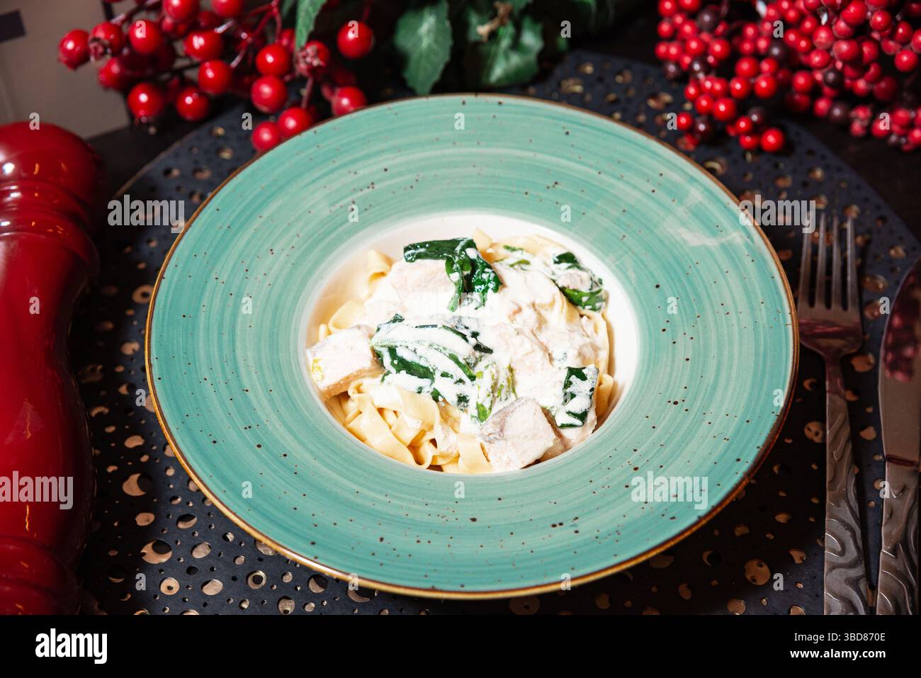 Tagliatelle servite con salsa bianca cremosa, teneri pezzi di pollo e spinaci freschi, placcati in un recipiente turchese. Foto Stock