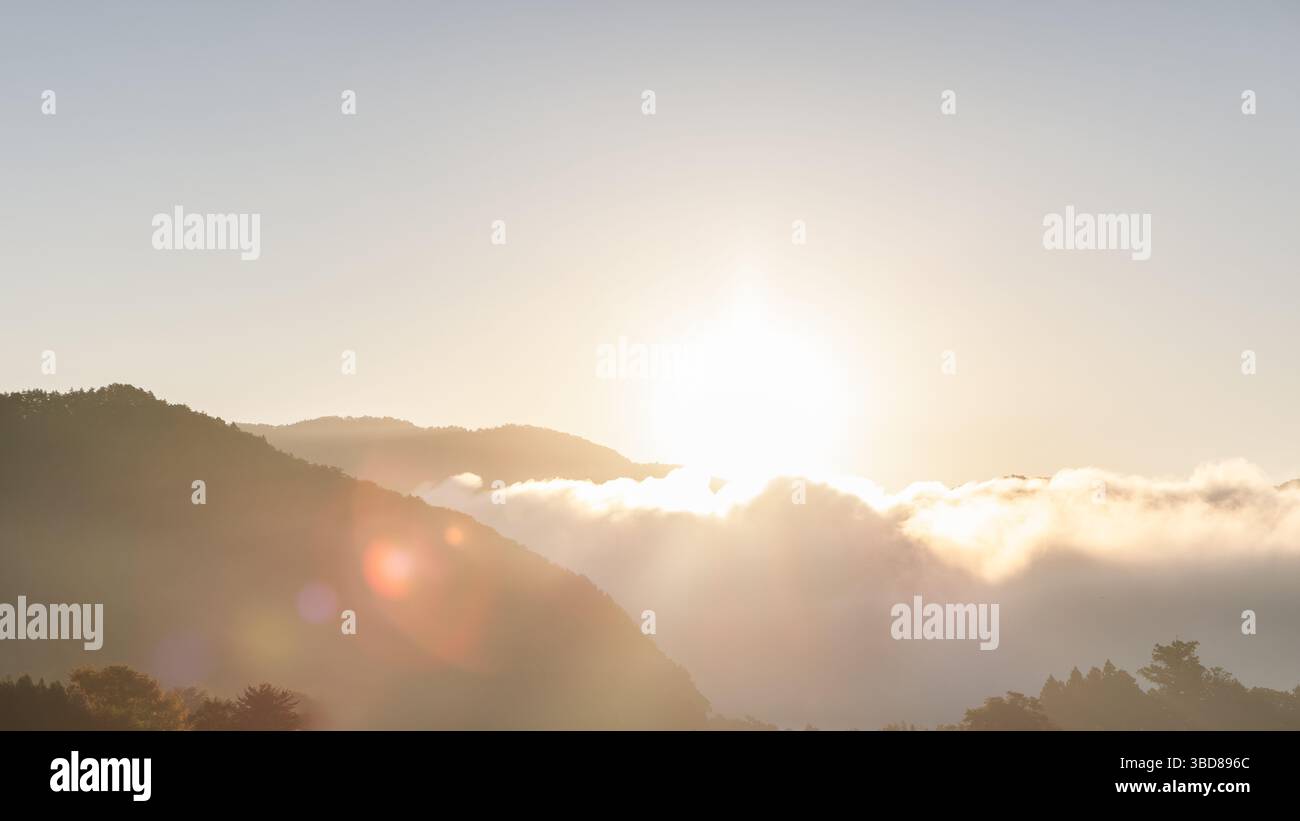 I raggi del sole nascente illuminano le nuvole che si spostano sopra le montagne, creando un gioco da sogno di luce e nebbia nell'aria frizzante del mattino Foto Stock