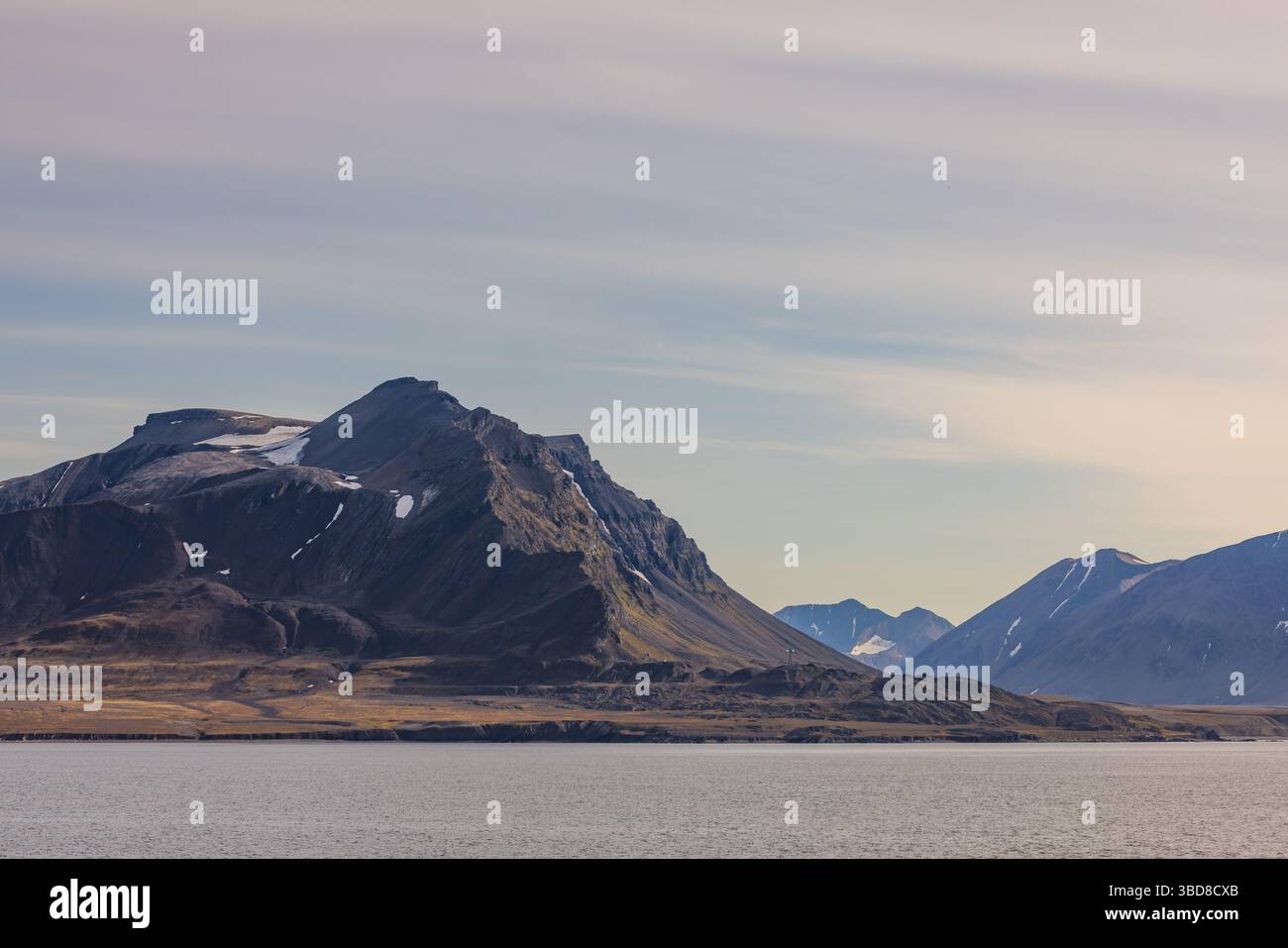 Le aspre montagne artiche si estendono lungo la costa delle Svalbard sotto i pastello cieli estivi, con macchie di neve aggrappate a ripidi pendii. Foto Stock