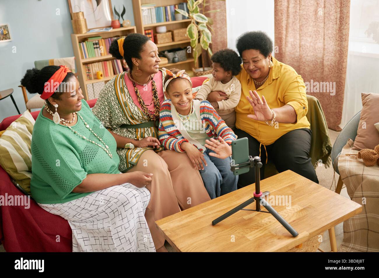 La famiglia Black multigenerazionale si è riunita per la configurazione delle videochiamate con il telefono su treppiede, sorridendo mentre chiacchierava e agitava la fotocamera nel vivo del roo Foto Stock