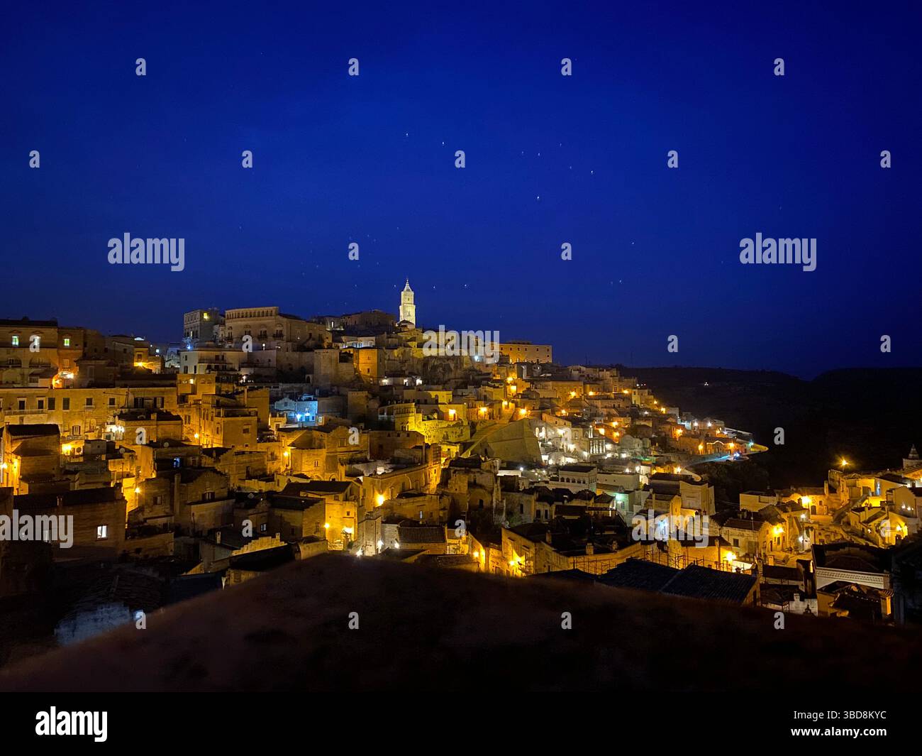 Paesaggio urbano di Matera che brilla di notte, antiche abitazioni in pietra scintillanti sotto il cielo stellato della Basilicata, rivelando fascino storico Foto Stock