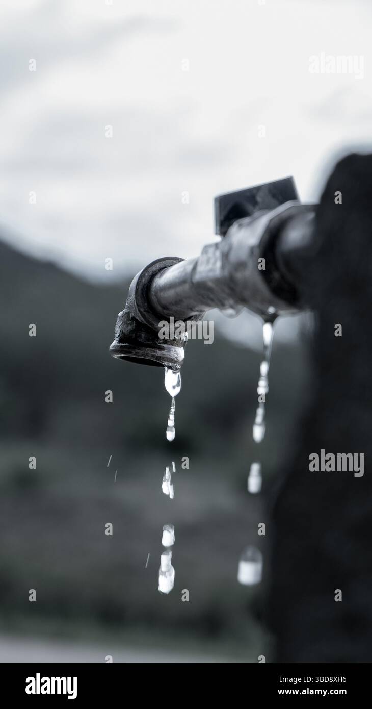 Primo piano di gocciolamento d'acqua dal vecchio rubinetto che simboleggia la scarsità e la conservazione Foto Stock