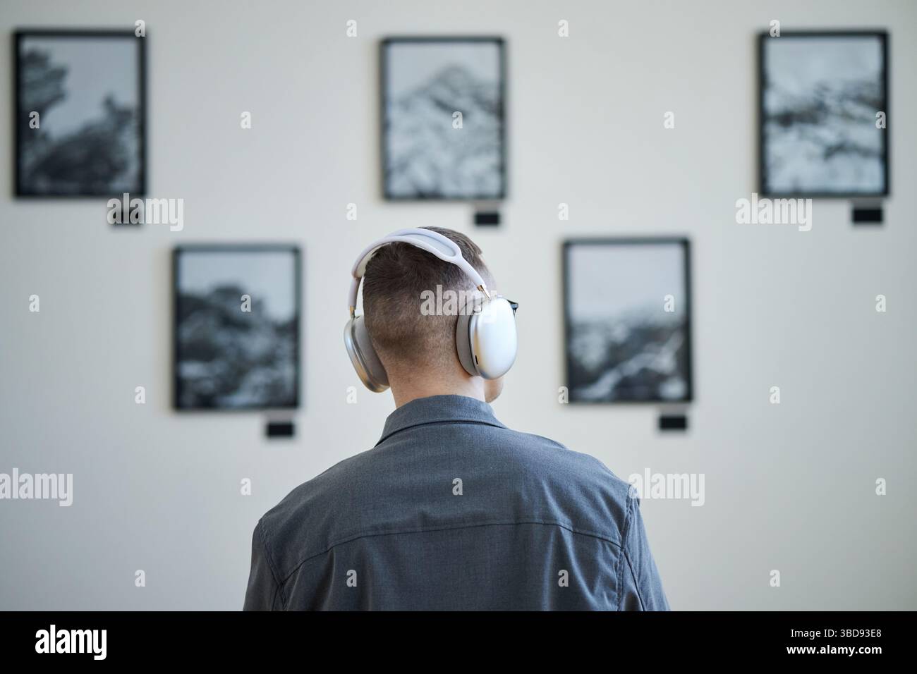 Persona che indossa le cuffie che guarda un'installazione artistica con fotografie a parete. Cuffie che indicano un'esperienza guidata coinvolgente con mostre d'arte Foto Stock