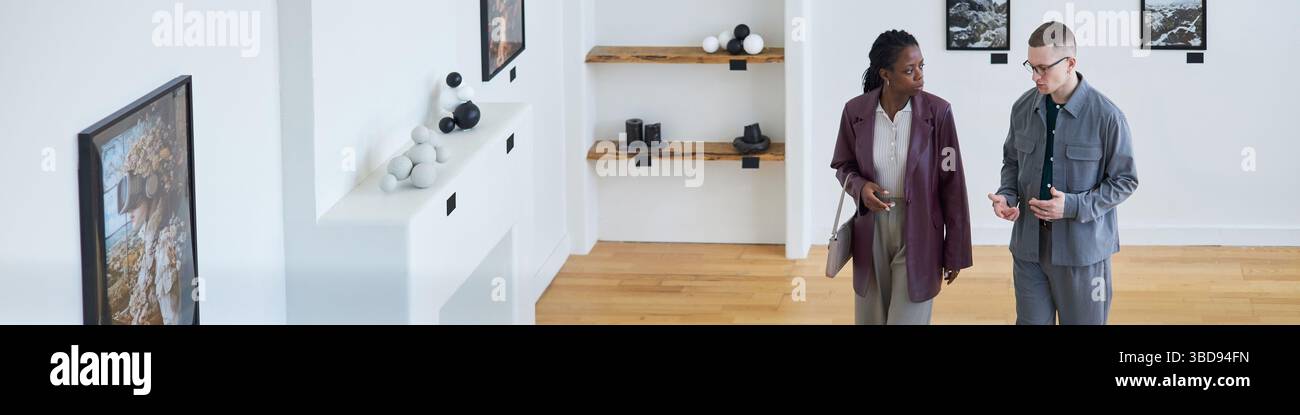 Fai un salto con due persone per esplorare la galleria d'arte moderna, discutere le mostre e guardare le immagini incorniciate sulle pareti. Scaffali con oggetti artistici esposti i Foto Stock