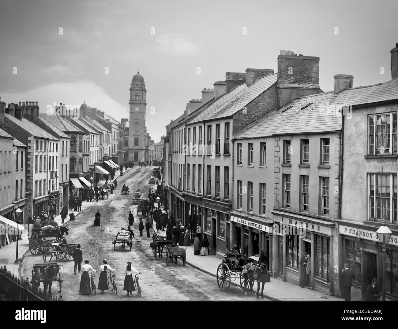 Una fotografia dei primi anni del XX secolo di negozi e acquirenti in Church Street a Enniskillen, la più grande città della contea di Fermanagh, Irlanda del Nord. In cima si può vedere la torre del municipio, progettata da William Scott e completata nel 1901. Foto Stock