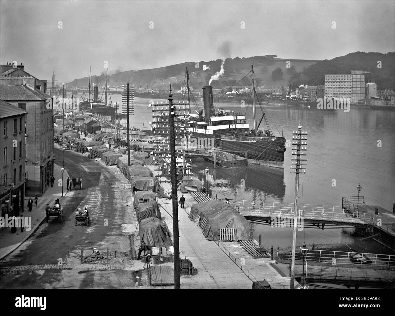 Una fotografia dei primi anni del XX secolo dei (South) Quays che costeggiano il fiume Suir mentre scorre attraverso Waterford City, in Irlanda. Nei primi anni '1700, il consiglio comunale abbatté le mura che si affacciano sul fiume e usa i resti per rendere le banchine più ampie e più adatte al commercio. I mercanti si trasferirono rapidamente e Waterford divenne un importante porto irlandese e un importante creatore di posti di lavoro in città. Le merci sono state scaricate, caricate e trasportate a mano lungo le banchine. Foto Stock