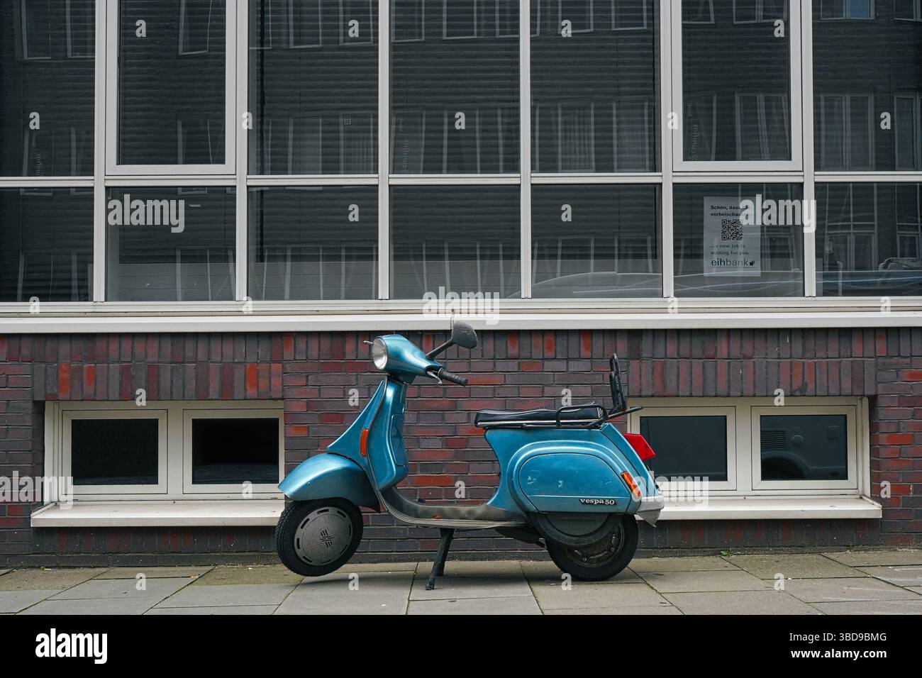 Vespa 50 blu d'epoca parcheggiata contro la moderna facciata in mattoni e vetro ad Amburgo, Germania. Foto Stock